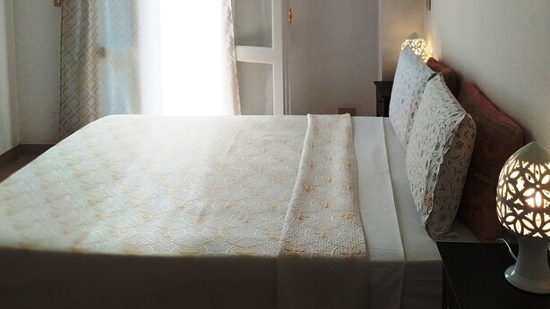 A bedroom with a bed, a nightstand, a wall-mounted lamp, and a window with curtains. - BnB 95mo (Lecce)