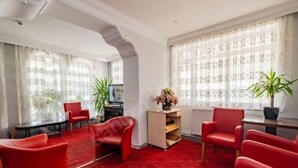 Ein Hotelzimmer mit rotem Teppich, roten Sesseln, einem Fernseher und zwei Blumentöpfen.