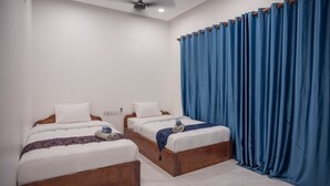 Habitación de hotel con dos camas, ventilador de techo y un gran ventanal con cortinas azules.