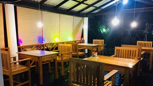 Un comedor interior con mesas y sillas de madera, un pastel pequeño en una mesa y luces de colores en la pared.