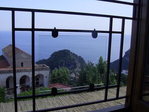 A view from a window with a metal grid, overlooking a coastal area with buildings and a hill. - Casa Falcone B&B (Scala)
