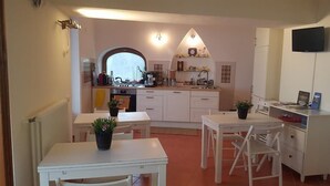 Cocina compacta con armarios blancos, una mesa de comedor con sillas y un televisor montado en la pared.