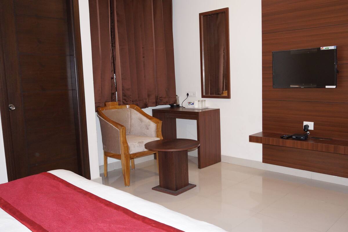 A hotel room with a bed, a wooden chair, a small table, a TV mounted on the wall, and a wooden cabinet.