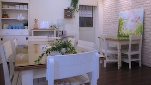 Zona pranzo con tavolo in vetro circondato da sedie bianche, parete in mattoni bianchi e un dipinto decorativo.
