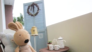 Un peluche su una sedia, un tavolino con teiera e tazze, e un portone azzurro decorato con un ghirlanda.