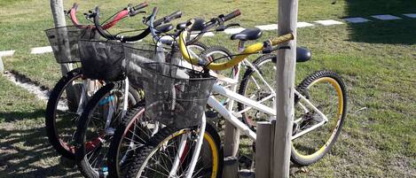 Bicicletas estacionadas en un área cubierta de césped, con un poste de madera y una valla de metal al fondo.