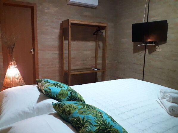 A hotel room with a bed, a wooden wardrobe, a television mounted on the wall, and a hanging light fixture.