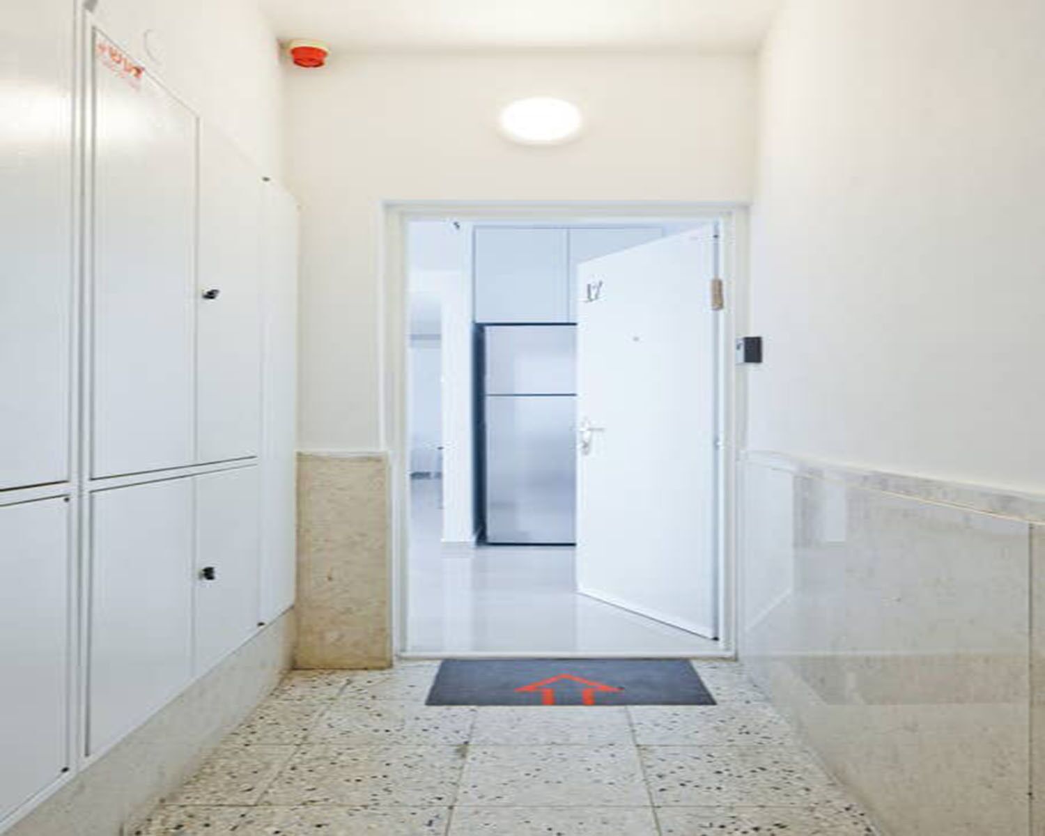 A narrow hallway with lockers on one side and a door leading to a room.
