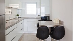A modern kitchen with white cabinets, a stainless steel sink, and a black dining table with two chairs. - 3BR Apt Beach View Best Loc Bat-Yam (Bat Yam)