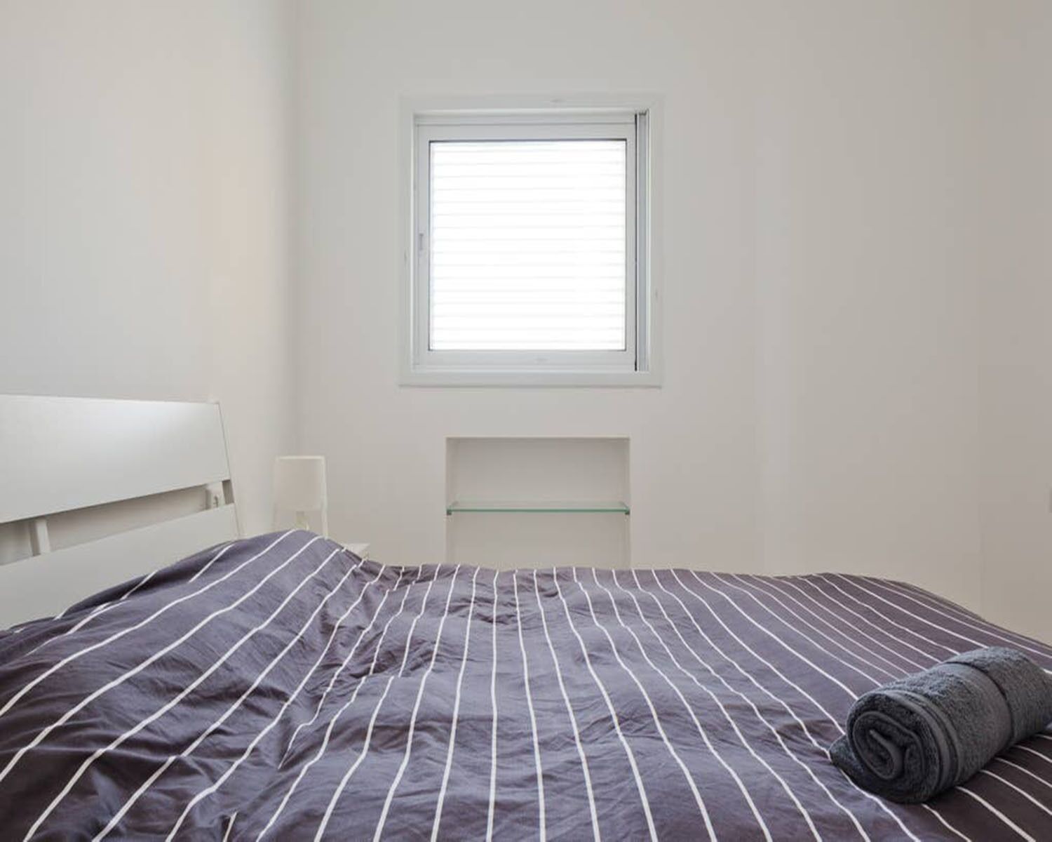 A bedroom with a bed, a window, and a shelf.