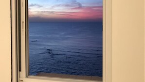 A window with a view of the ocean during sunset, featuring a clear sky and calm sea. - 3BR Apt Beach View Best Loc Bat-Yam (Bat Yam)