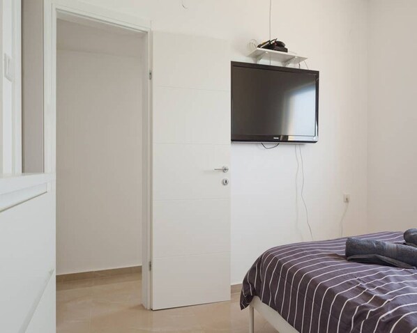 A bedroom with a bed, a television mounted on the wall, and a door leading to another room.