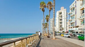 A wooden boardwalk with benches, palm trees, and a view of the ocean. - 3BR Apt Beach View Best Loc Bat-Yam (Bat Yam)