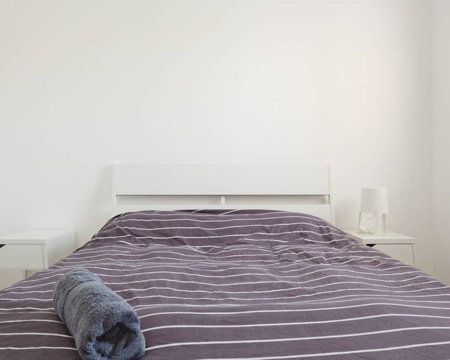 Ein ordentlich bezogenes Bett mit einem gestreiften Bettüberwurf, einem weißen Kopfteil und einem Nachttisch mit Lampe.