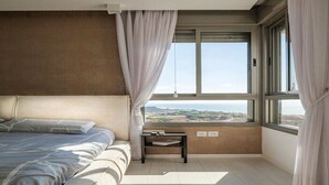 A bedroom with a bed, a nightstand, and a window with curtains. - Luxury Mini Penthouse Sea View Best Loc (Bat Yam)