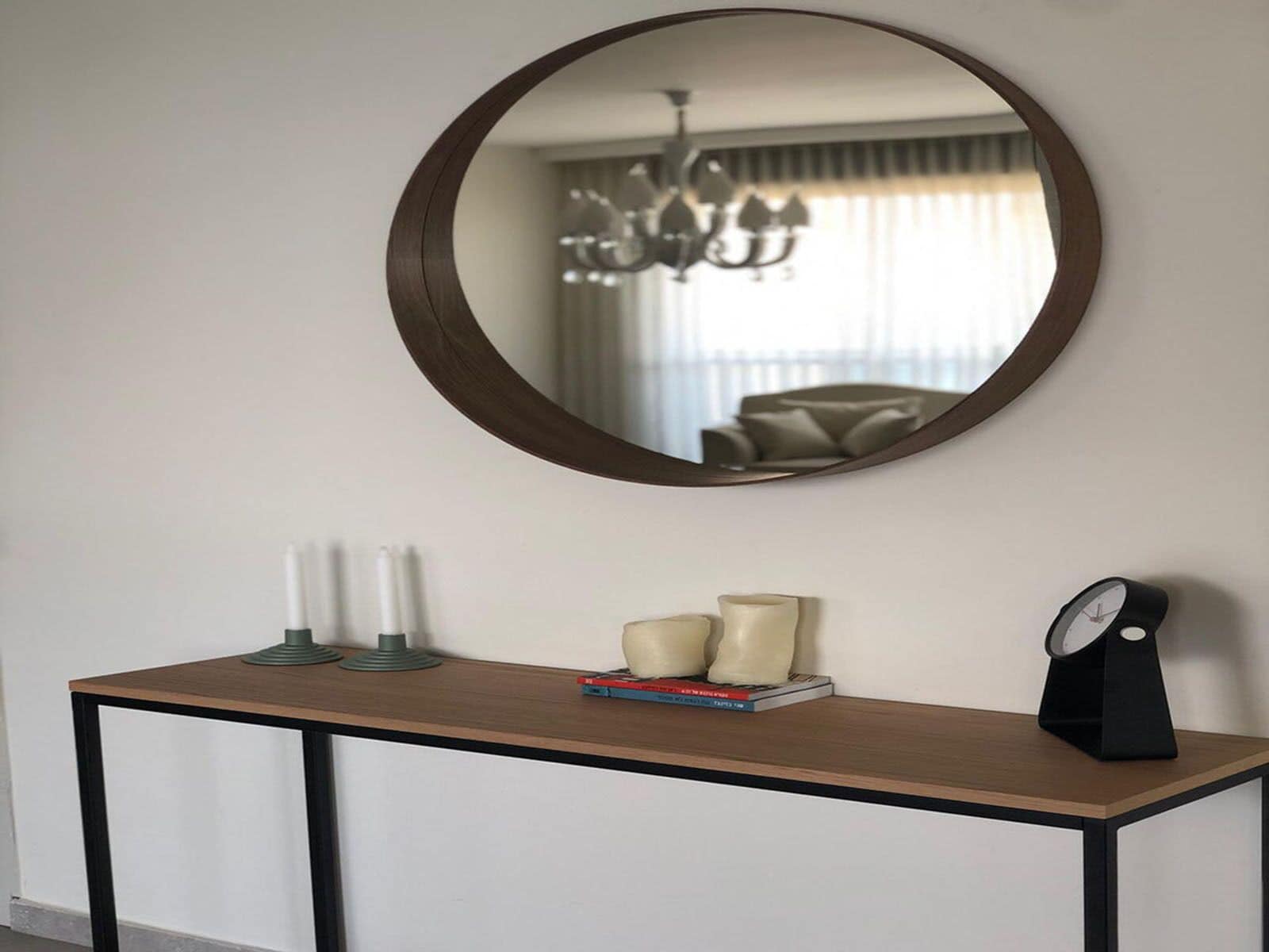 A round mirror on a wall above a wooden console table with candles and a clock.