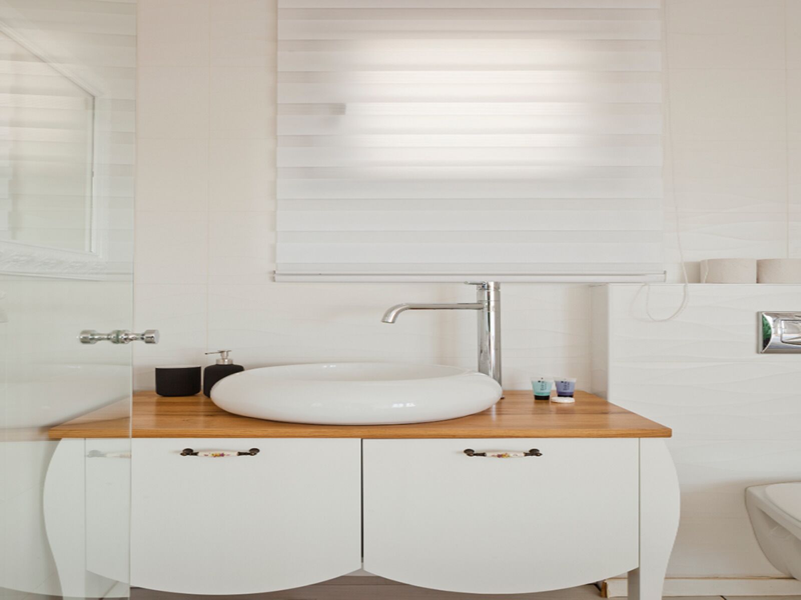 A bathroom with a white sink, wooden countertop, and white cabinets.