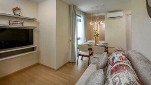 A modern living room with a flat-screen TV, a dining area with a table set for two, and a sofa with patterned cushions. - Splendid Sea View Resort (Karon)