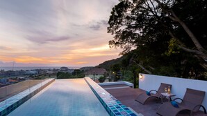 A rooftop infinity pool with a view of the city at sunset, lounge chairs, and a small table with a bottle. - Splendid Sea View Resort (Karon)