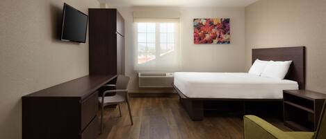 Habitación de hotel con cama, escritorio, silla, televisor y ventana con vista a la ciudad.