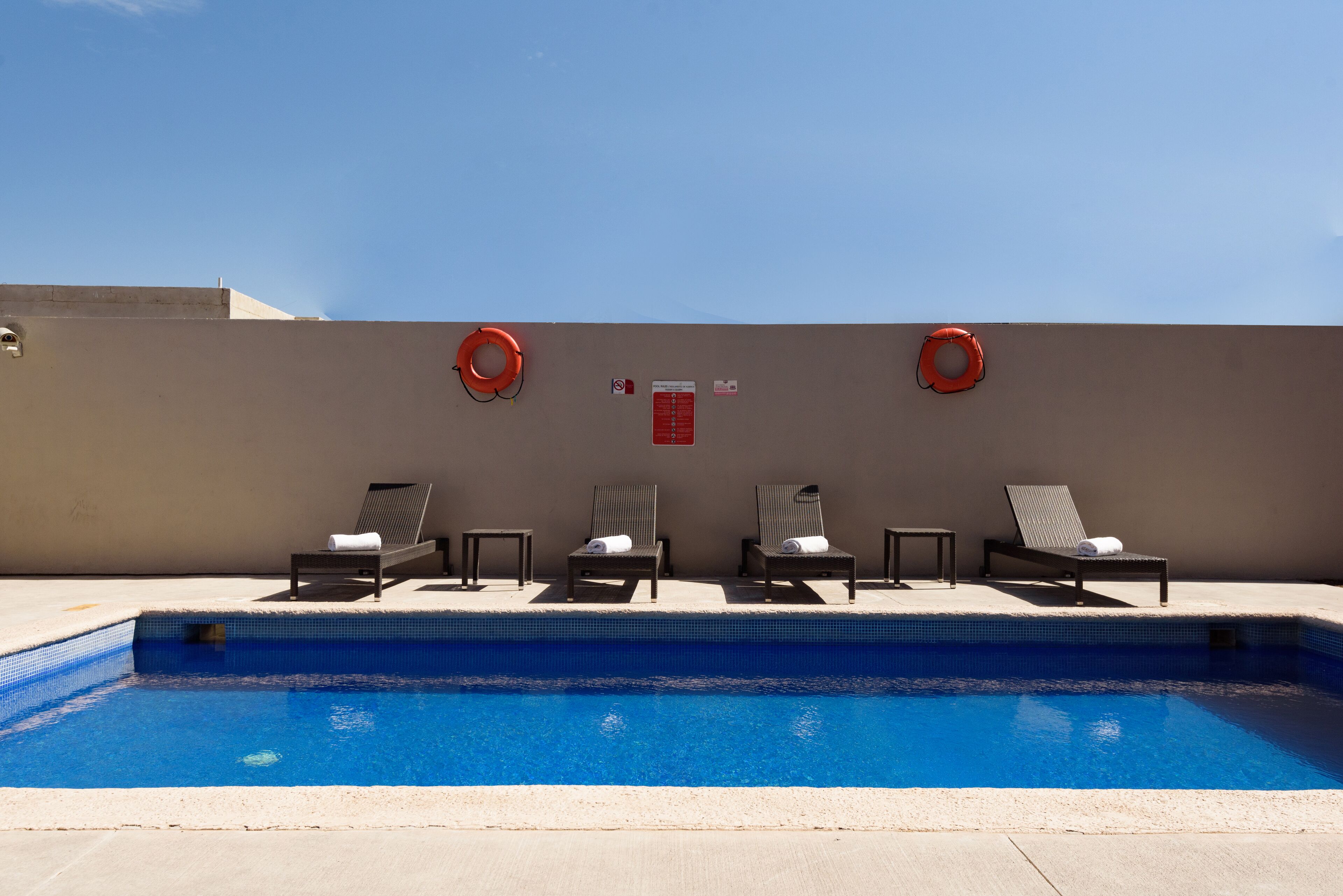 A swimming pool with four lounge chairs and two life rings on a sunny day.
