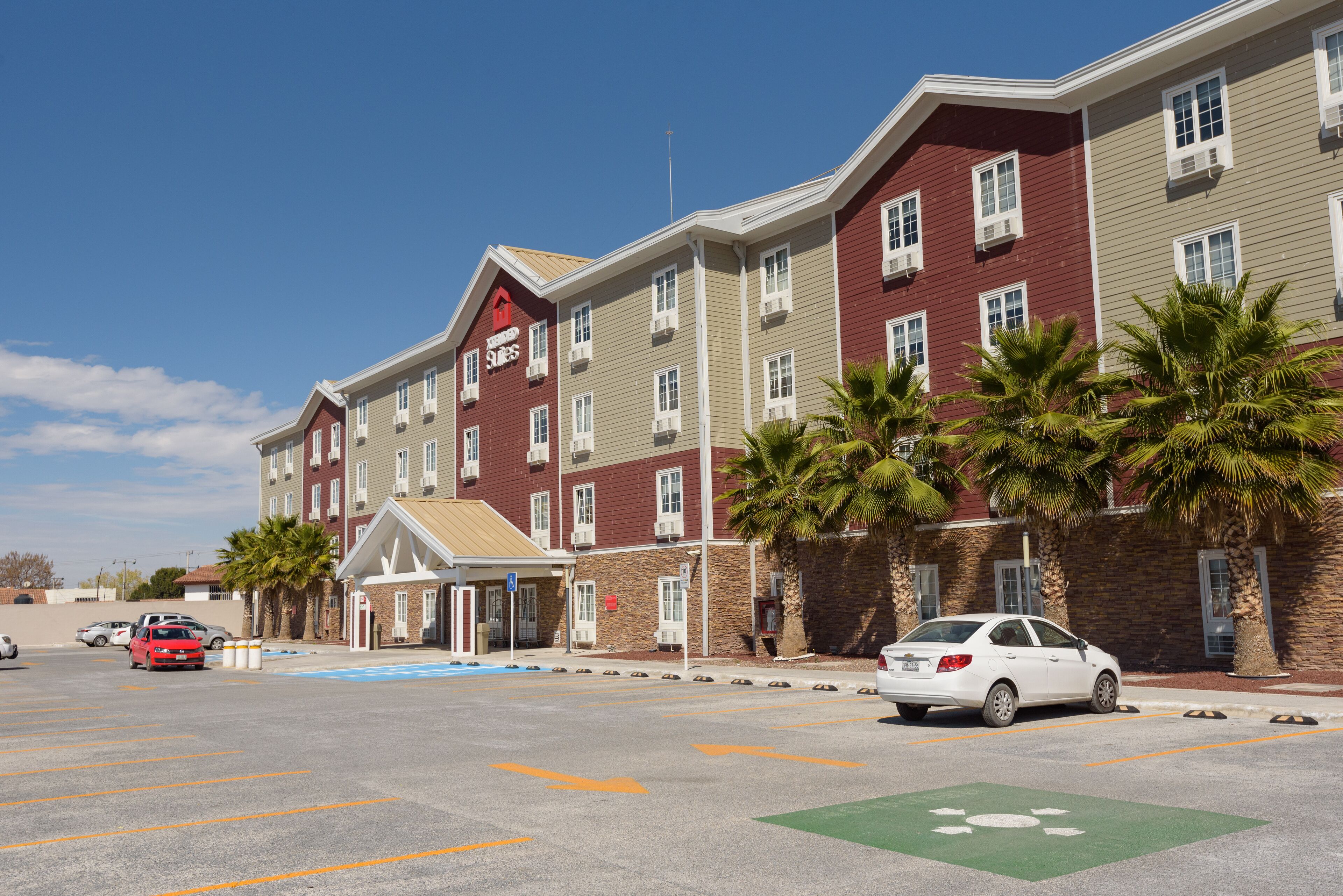 A multi-story hotel with a red and beige facade, a covered entrance, and palm trees in front.
