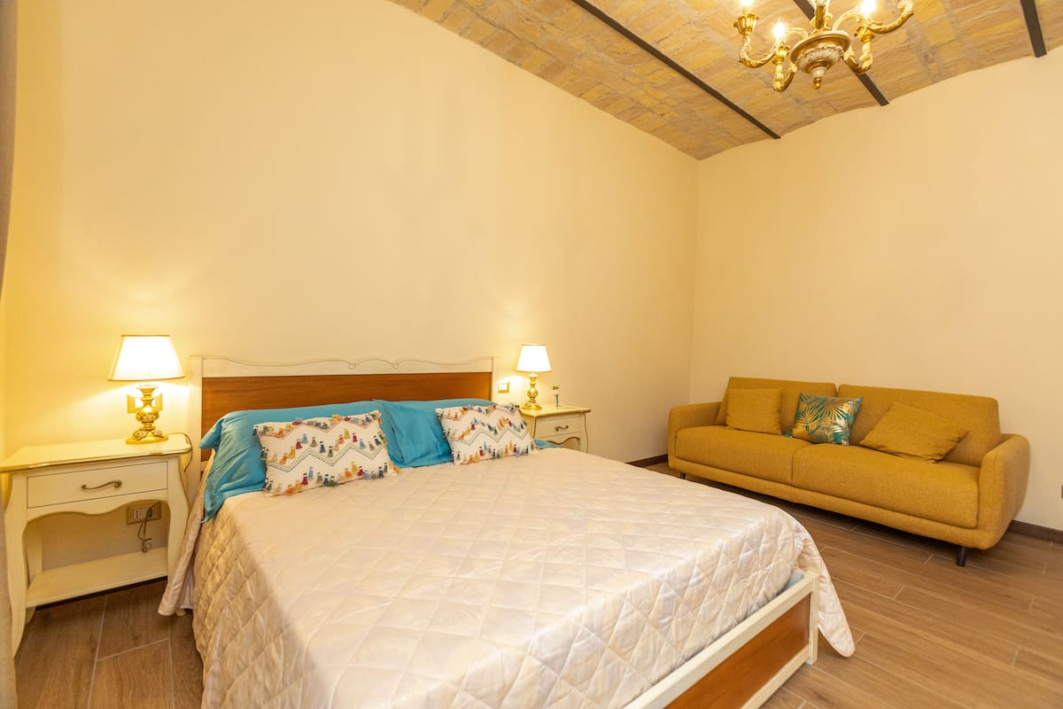 Une chambre à coucher avec un lit, deux tables de chevet avec des lampes, un canapé et un lustre.