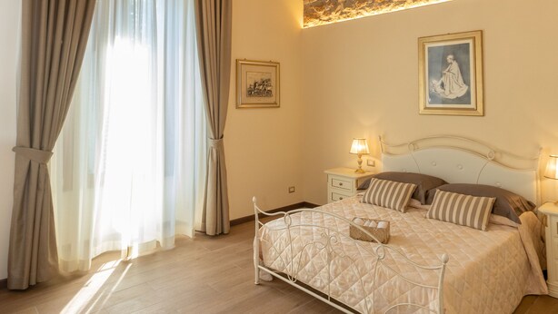 A bedroom with a large bed, a chandelier, a brick wall, and a window with curtains. - Kings Home In Rome (Rome)