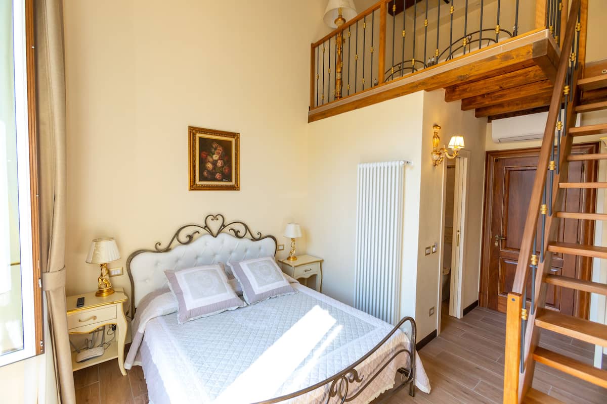 Une chambre à coucher avec un lit, des tables de chevet, un tableau au mur, un radiateur et un escalier en bois.