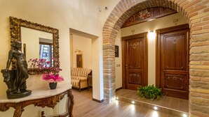 A hallway with a marble table, a statue, and a mirror. There are two wooden doors and a brick archway. - Kings Home In Rome (Rome)