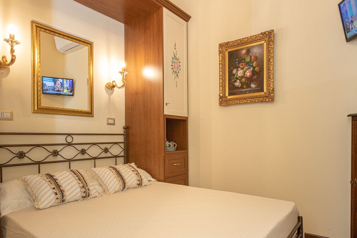 Une chambre à coucher bien rangée, avec un lit, une tête de lit en bois, un lustre, une télévision et un tableau encadré au mur.