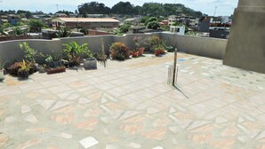 A rooftop terrace with a patterned tile floor, potted plants, and a metal pole.