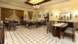 A spacious hotel room with a large dining area, a sofa set, a chandelier, and a ceiling fan.
