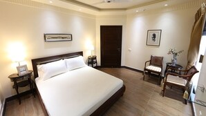 A hotel room with a large bed, two bedside tables with lamps, a ceiling fan, a door, and two chairs.