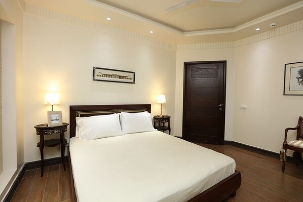 Habitación de hotel con una cama grande, dos mesitas de noche con lámparas, un cuadro enmarcado en la pared, una puerta y una silla.