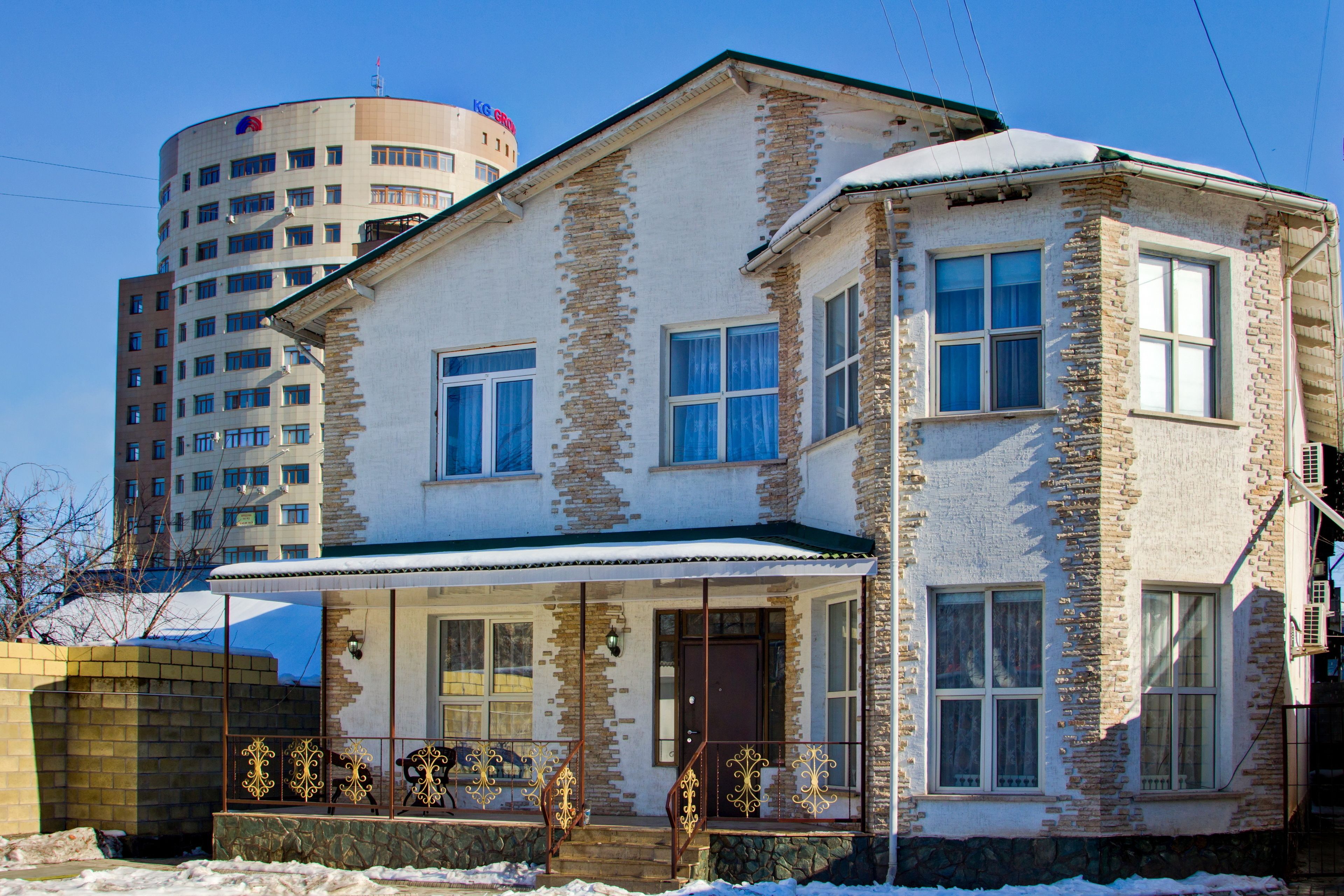 A two-story building with a stone facade, a balcony with ornate metal railings, and a snow-covered roof.