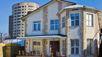 A two-story building with a stone facade, a balcony with ornate metal railings, and a snow-covered roof.
