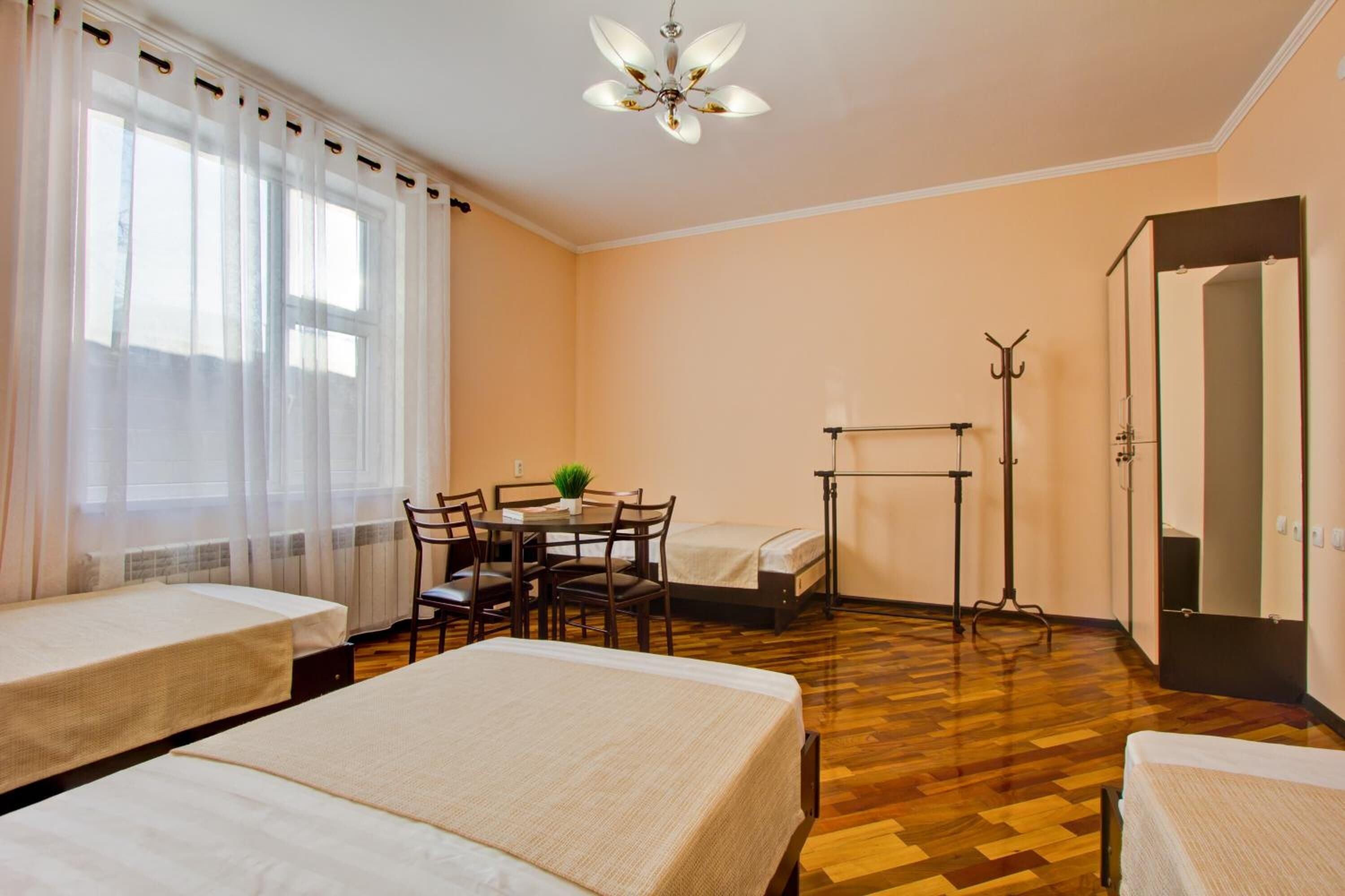 A hotel room with two beds, a table with chairs, a small table with a plant, a standing lamp, and a coat rack.