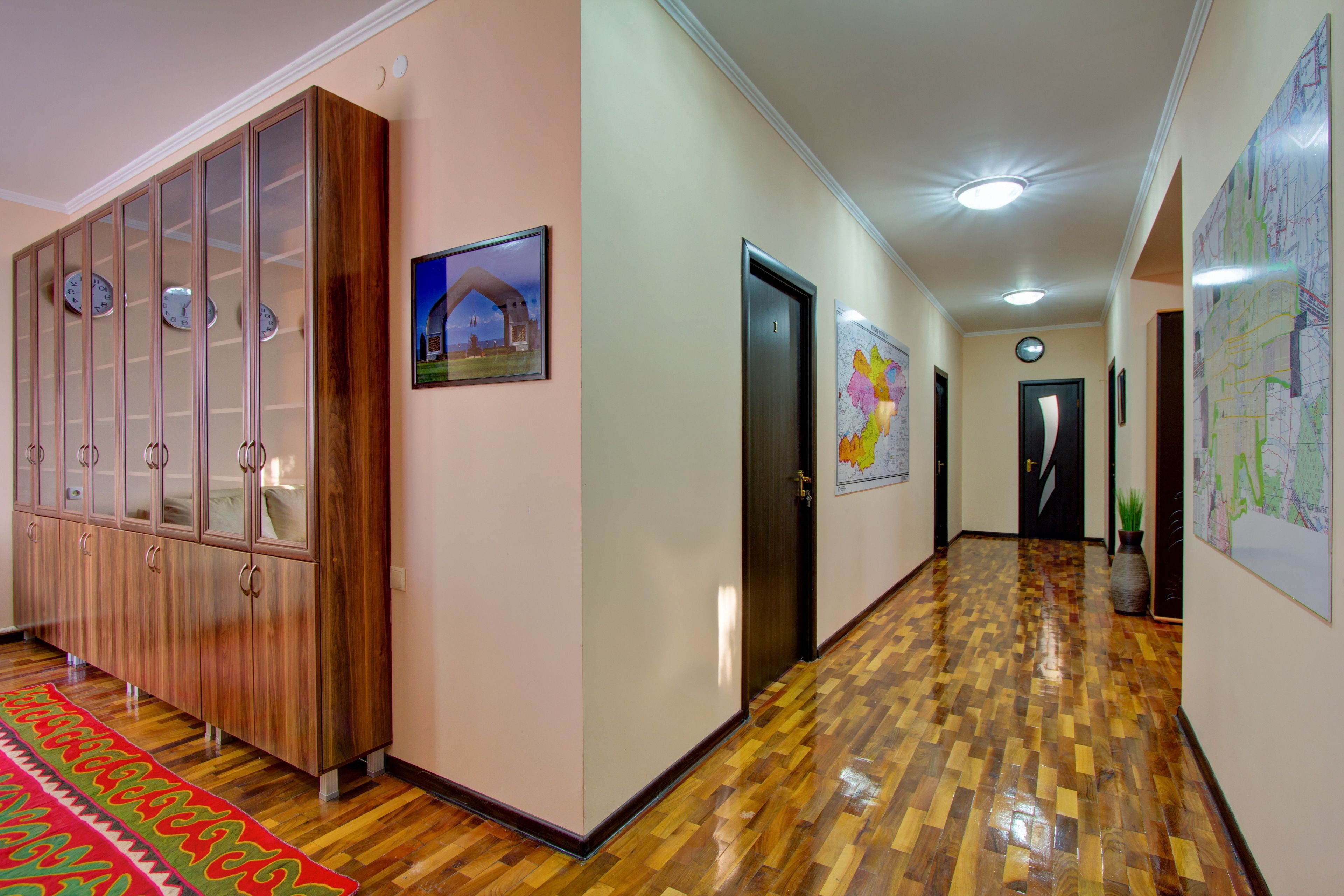 Un couloir doté d’un plancher en bois, d’une grande armoire aux portes en verre et d’un tapis rouge.