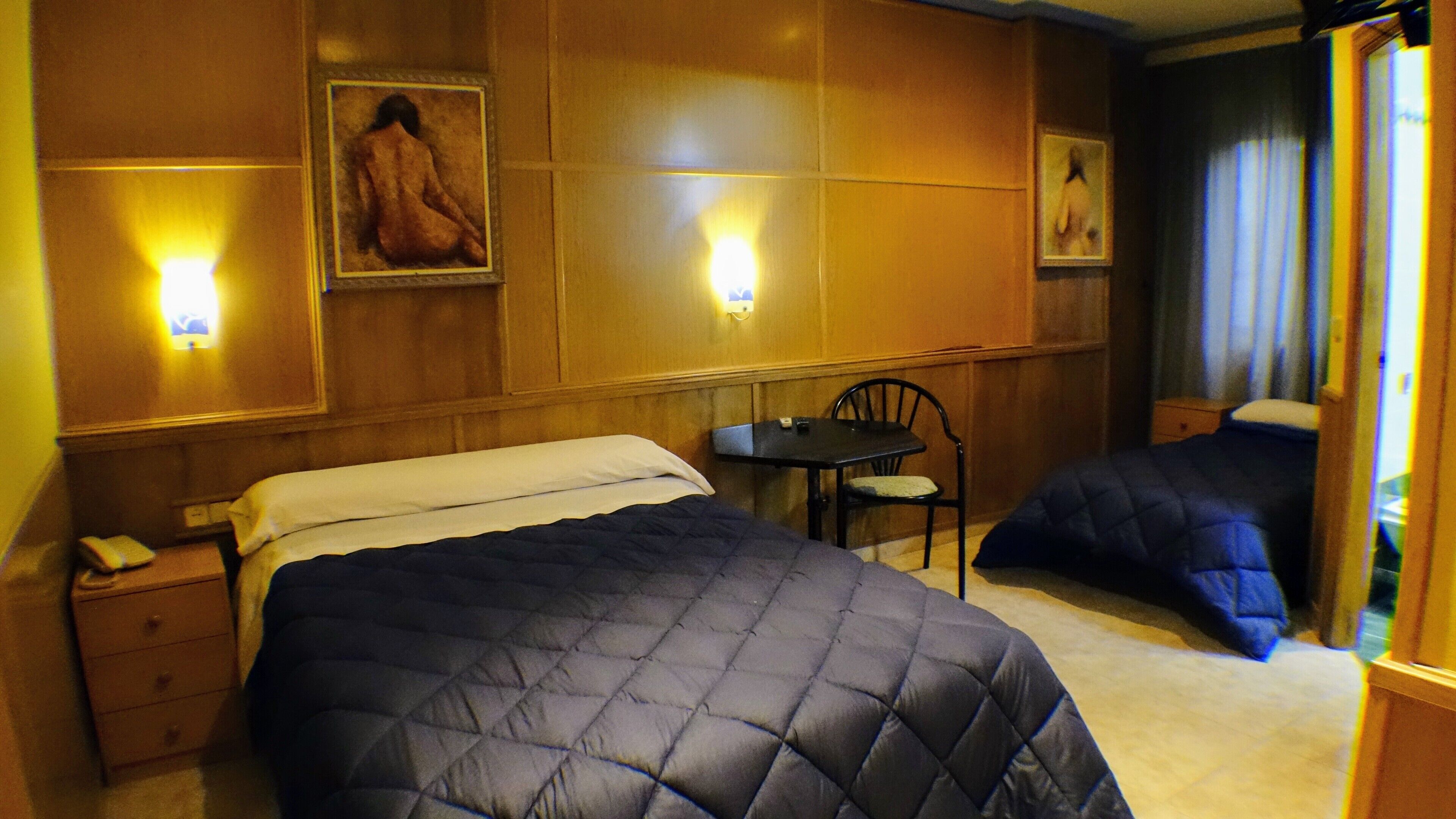 Ein Hotelzimmer mit zwei Betten, einem Schreibtisch, einem Stuhl und zwei Wandleuchten.