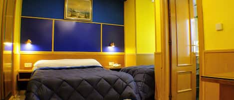 A hotel room with a bed, bedside tables, a nightstand, a wooden wardrobe, and a painting on the wall.