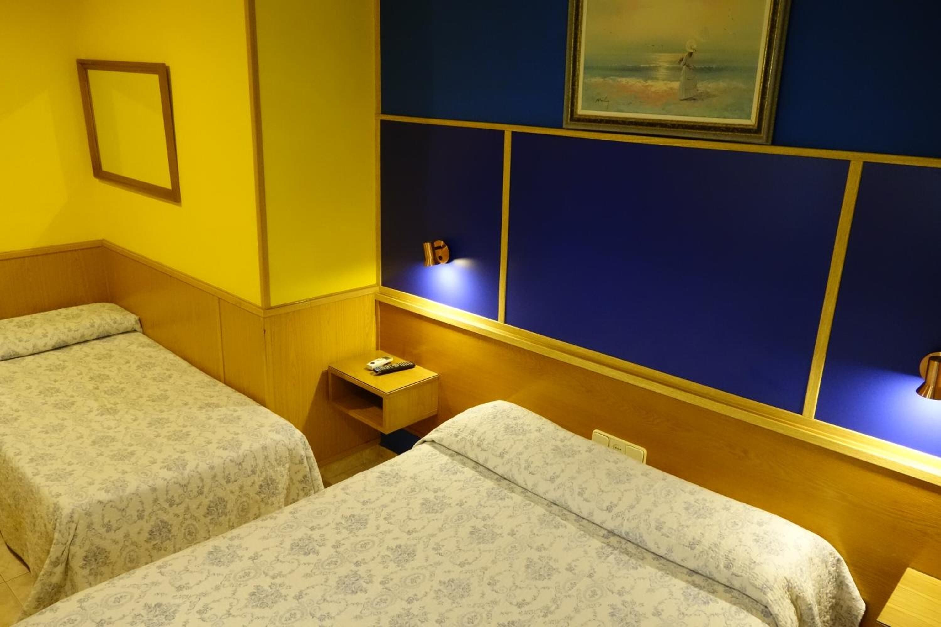 Une chambre d’hôtel avec deux lits, une petite table de chevet avec une lampe et un tableau au mur.