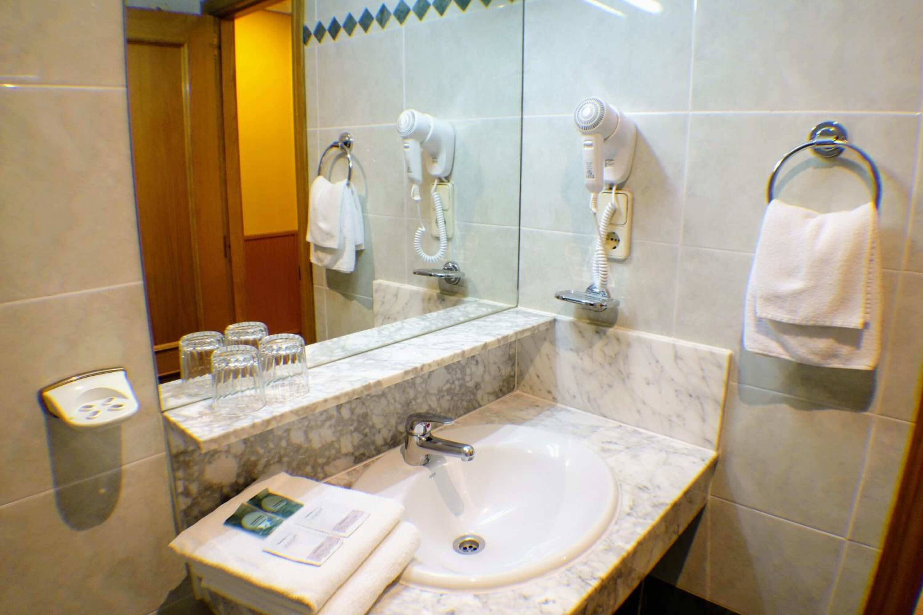 A bathroom with a marble sink, a mirror, a hairdryer, and a towel rack.