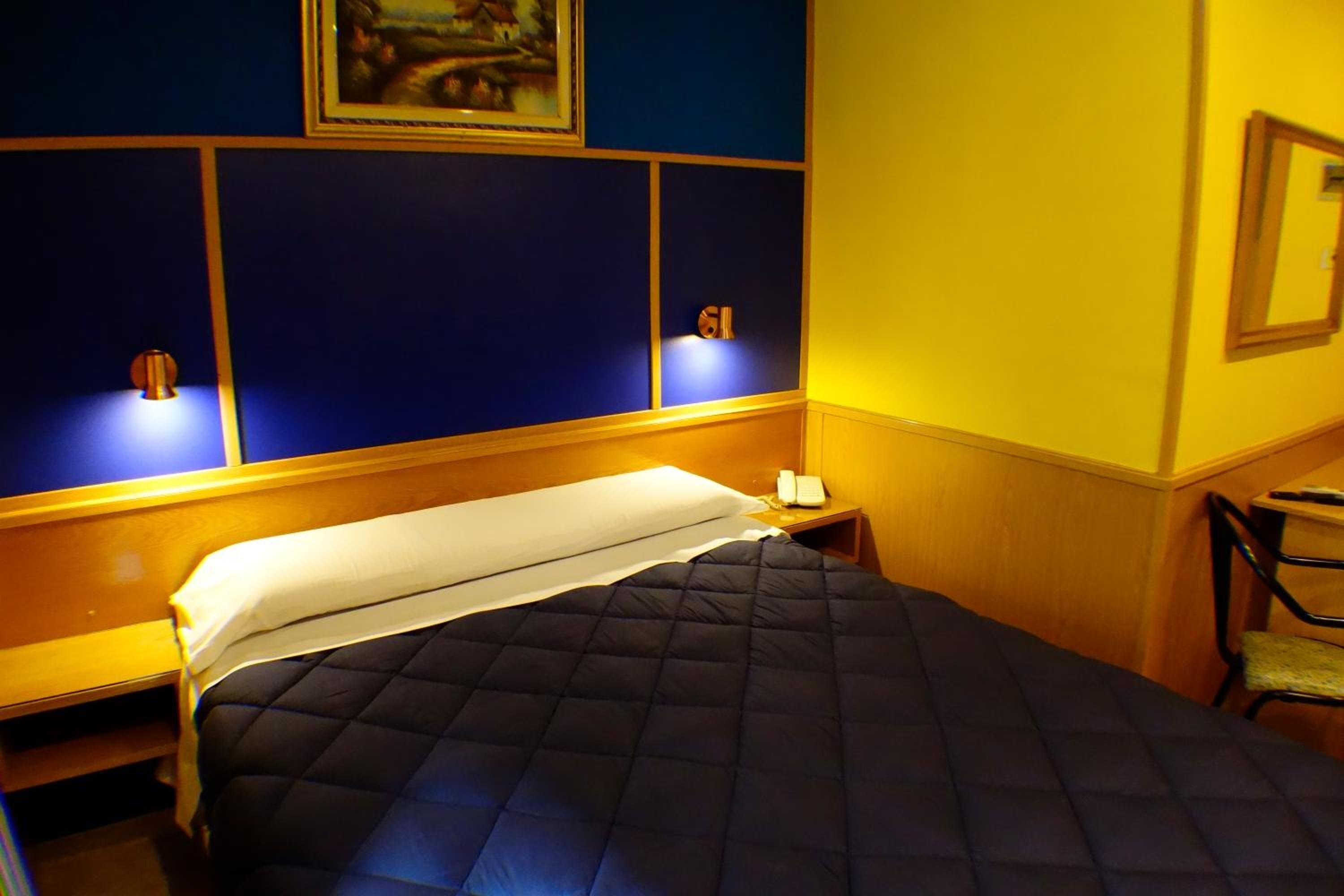 A hotel room with a bed, a bedside table, and a chair.