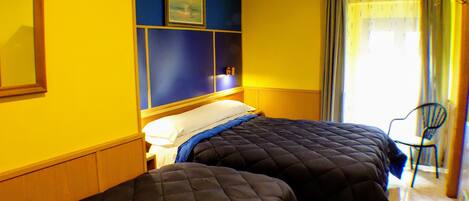 Habitación de hotel con dos camas, una pared azul decorativa, un cuadro y una silla cerca de la ventana.