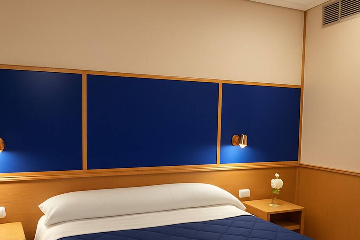 Una habitación de hotel con una cama grande, cabecera de madera y dos mesitas de noche con lámparas.