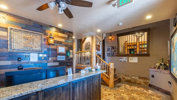 A reception area with a wooden counter, a ceiling fan, and a staircase leading to an upper level. - Zion Cliff Lodge (Hildale)