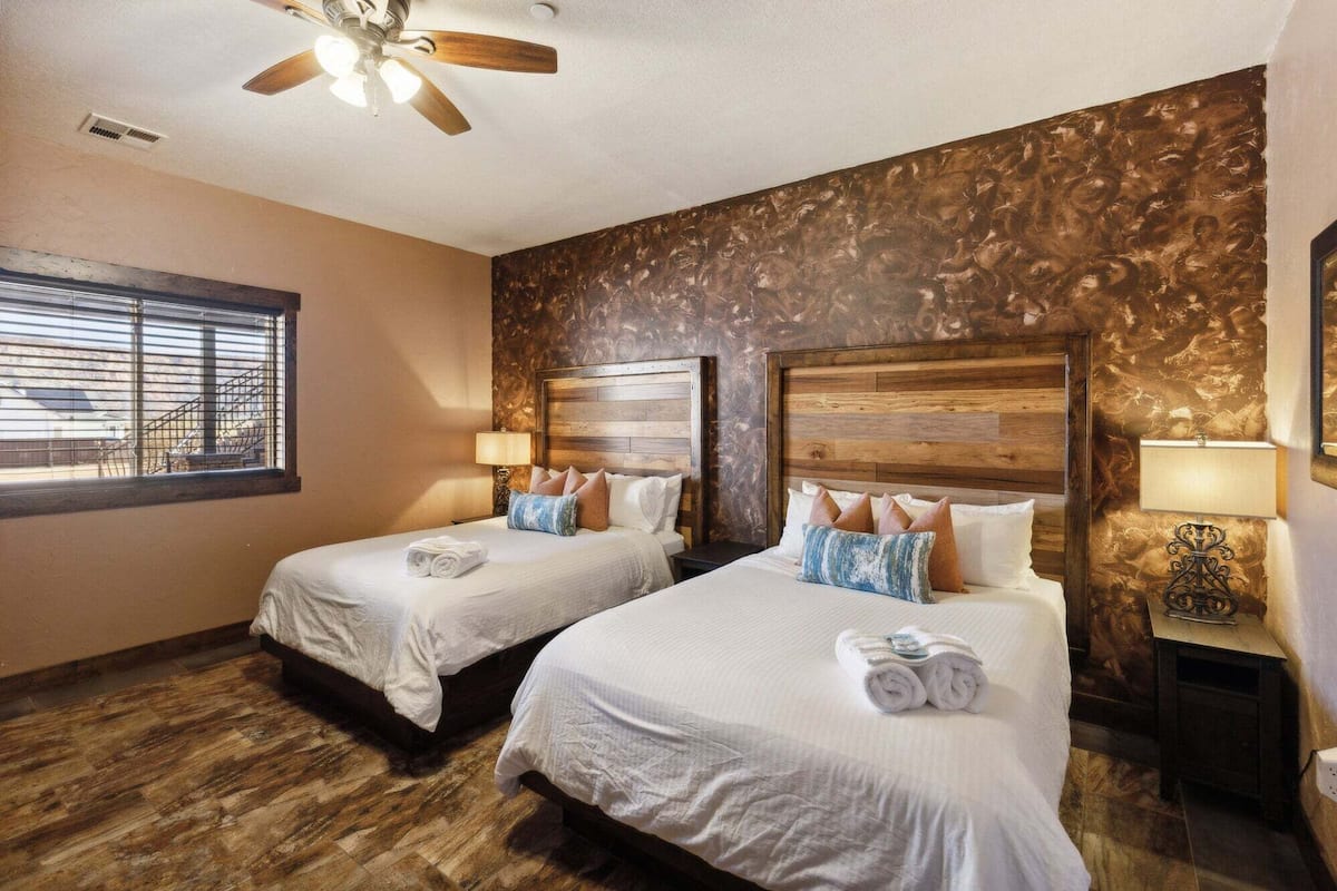 A hotel room with two beds, wooden headboards, and a ceiling fan.