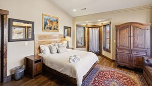 A bedroom with a wooden headboard, a large bed with multiple pillows, a ceiling fan, a wooden wardrobe, and a window with blinds. - Zion Cliff Lodge (Hildale)
