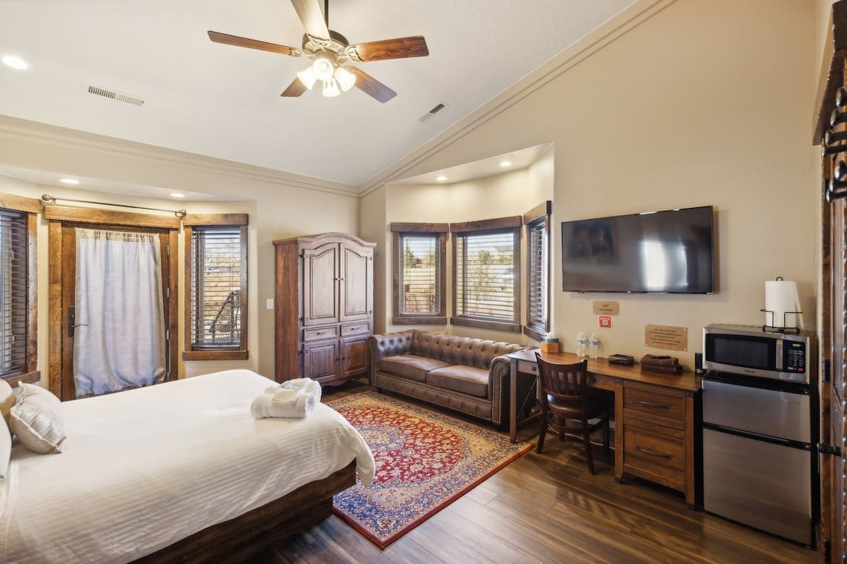 A hotel room with a bed, a desk, a chair, a television, and a refrigerator.